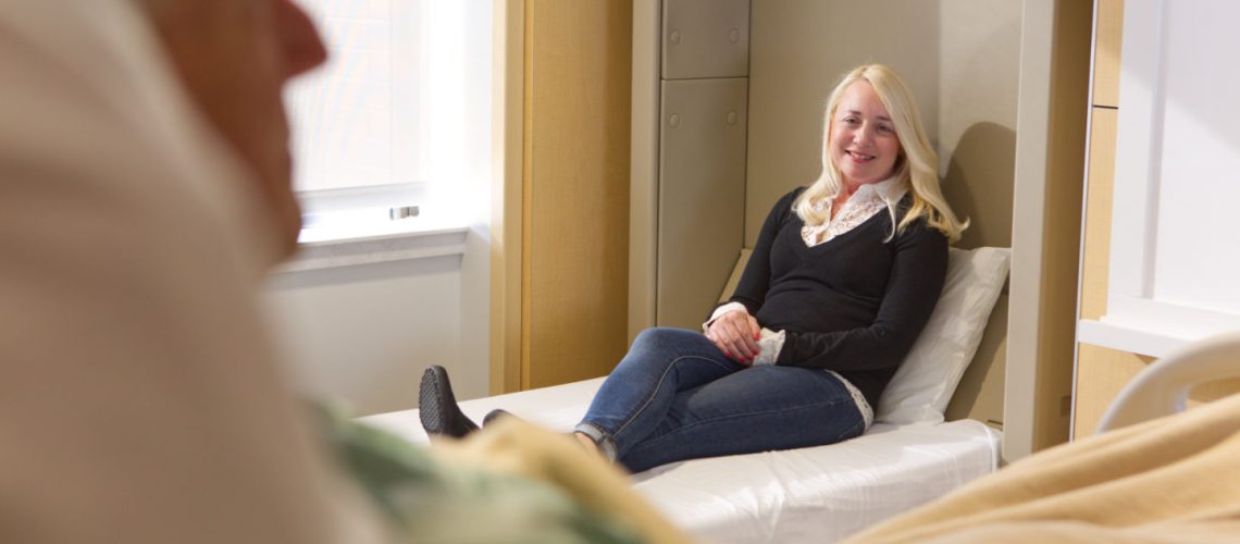 woman sitting on caregiver bed talking to father in hospital